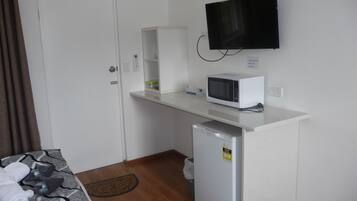 Een kleine kitchenette met een magnetron, een minibar, een aan de muur bevestigde televisie en een bed met handdoeken.
