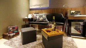 A modern living room with a sofa, ottomans, a coffee table with a bottle and glass, a television, and a bookshelf. - Hotel B7 Journey (TAIPEI)