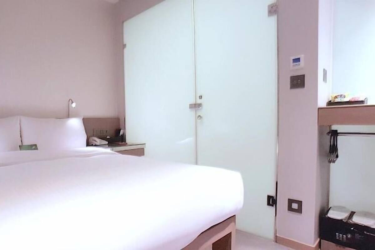 A hotel room with a bed, a wardrobe, a bedside table, and a mirror.