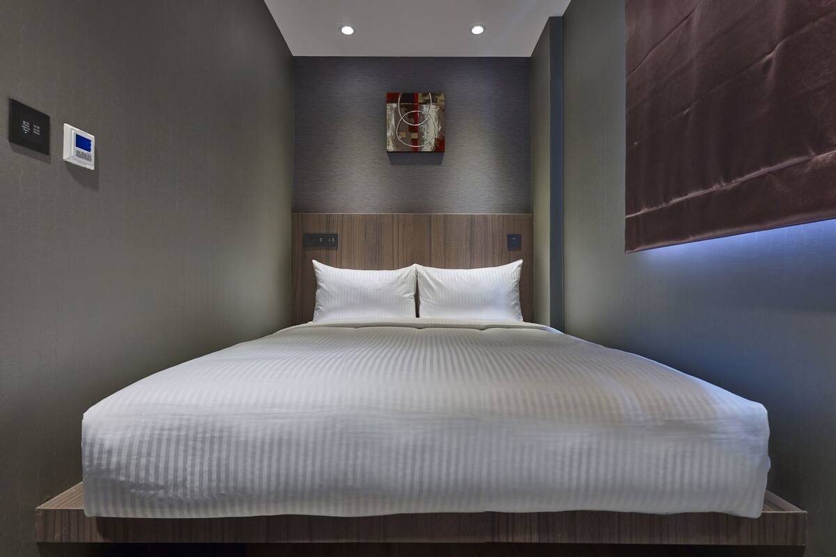 A modern hotel room with a large bed, a wooden headboard, and a wall-mounted artwork.