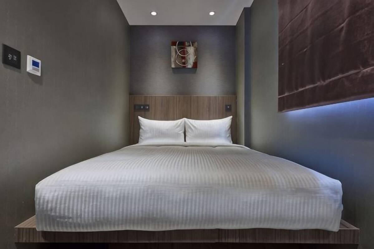 A modern hotel room with a large bed, a wooden headboard, and a wall-mounted artwork.