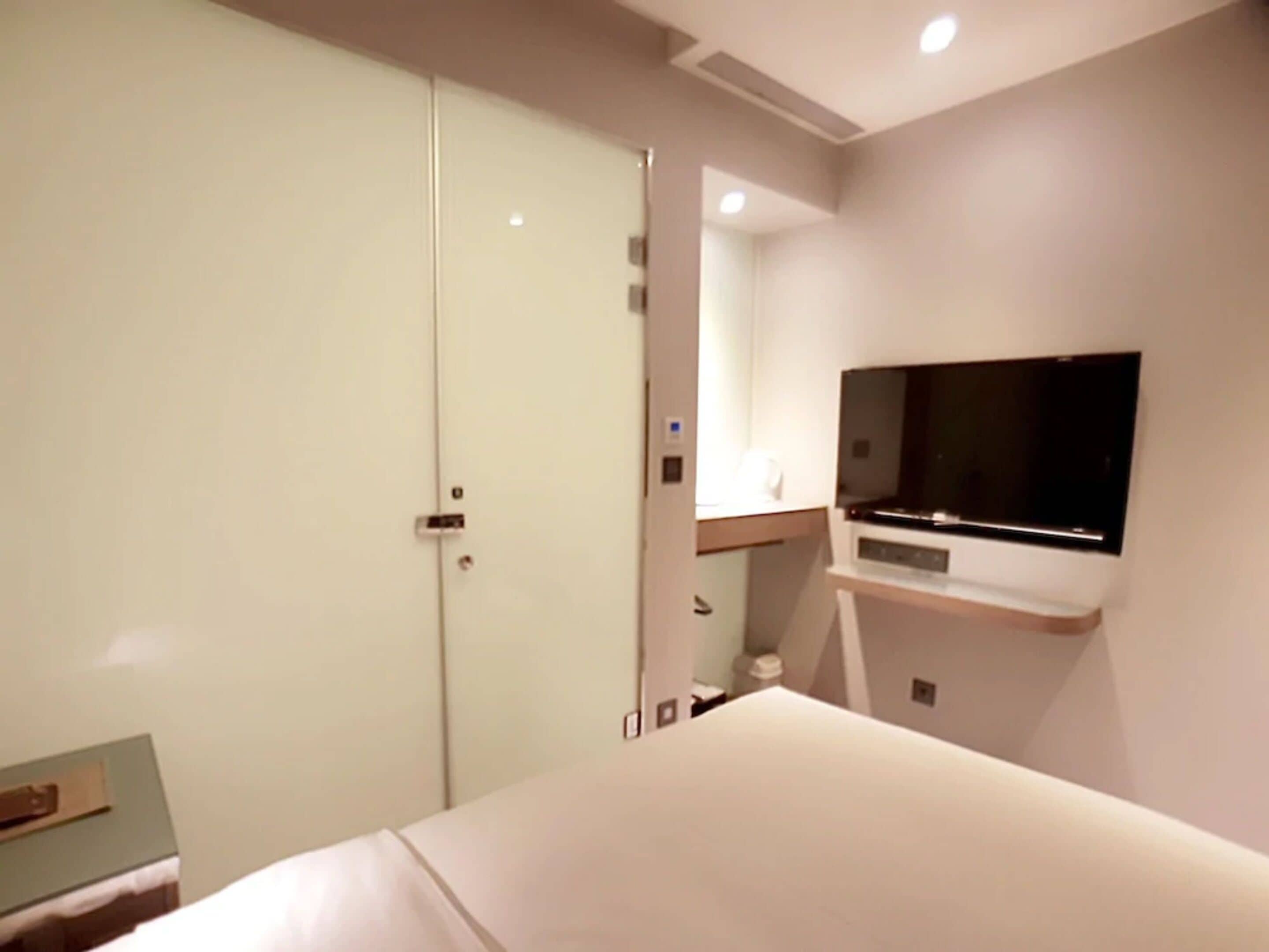 A modern hotel room with a bed, a TV mounted on the wall, and a wardrobe.