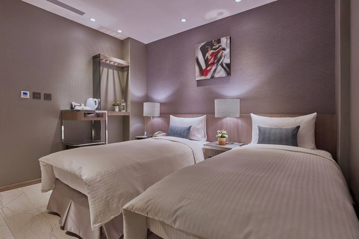A hotel room with two beds, a desk, a mirror, and a painting on the wall.