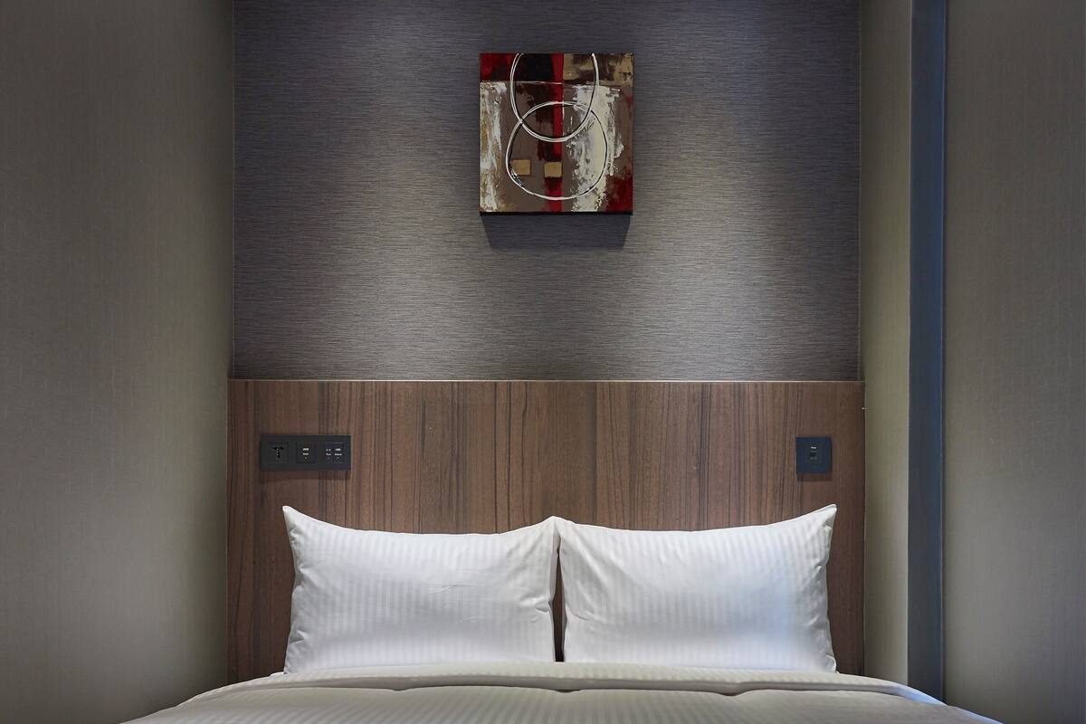 A modern hotel room with a large bed, a wooden headboard, and a wall-mounted artwork.