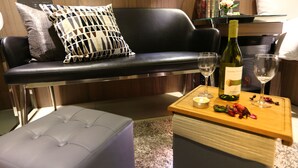 A modern living room with a black leather sofa, a white ottoman, and a wooden coffee table with a bottle of wine, glasses, and a candle. - Beauty Hotels Taipei Hotel B7 Journey (Taipei)