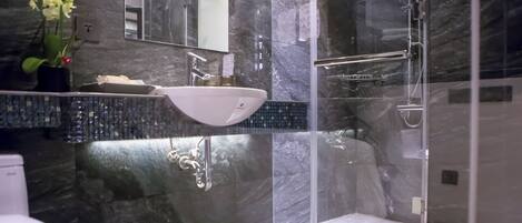 Une salle de bain moderne avec un pare-baignoire en marbre, un lavabo blanc, une douche à parois de verre et des toilettes.