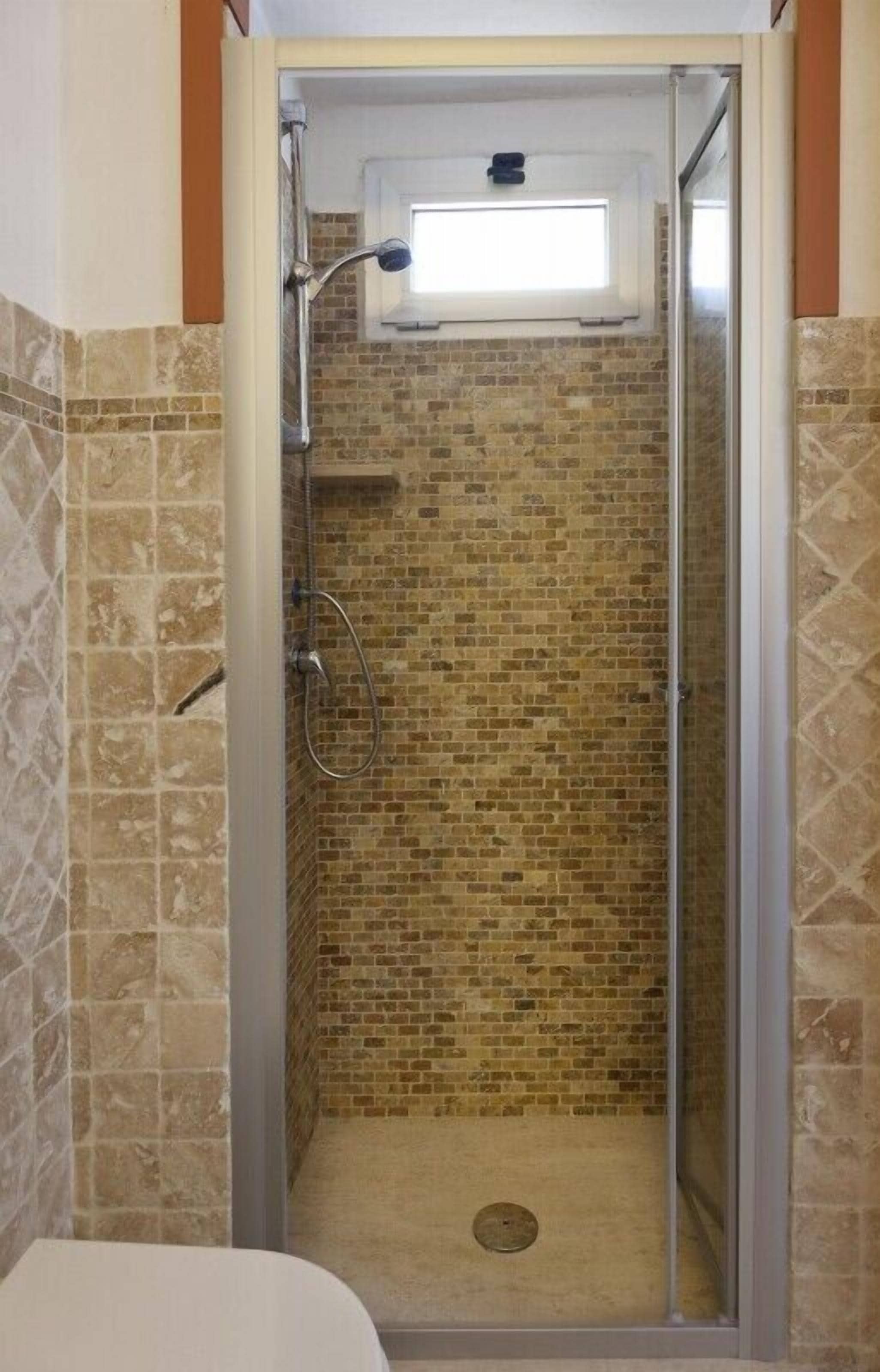 A shower with a glass door, a window above the shower, and a tiled wall.