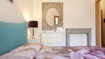 A bedroom with a bed, a dresser, a mirror, a lamp, and a fireplace.