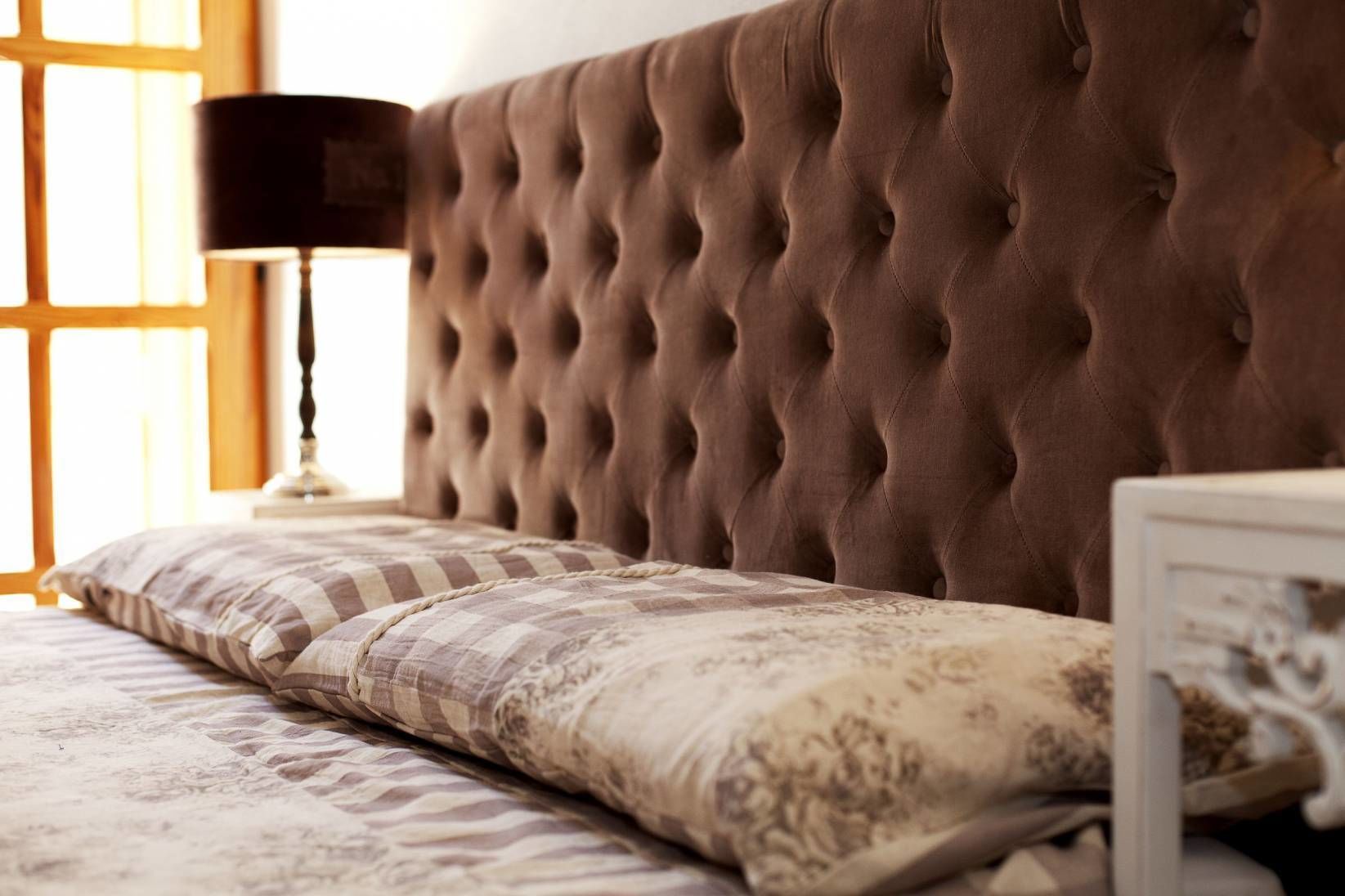 A tufted headboard, a lamp, and a patterned bedspread.