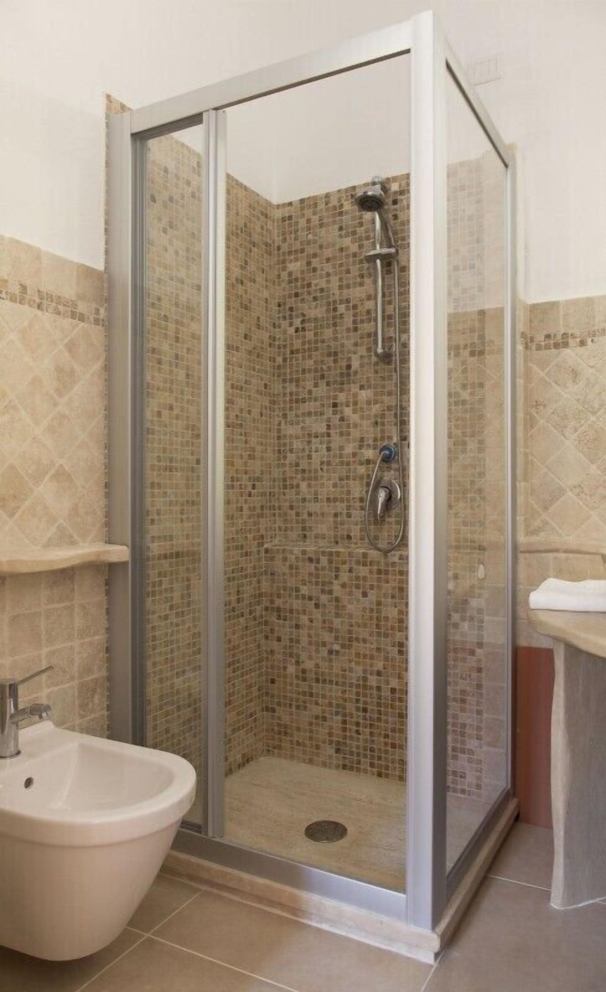A glass-enclosed shower with mosaic tile walls and a white sink.