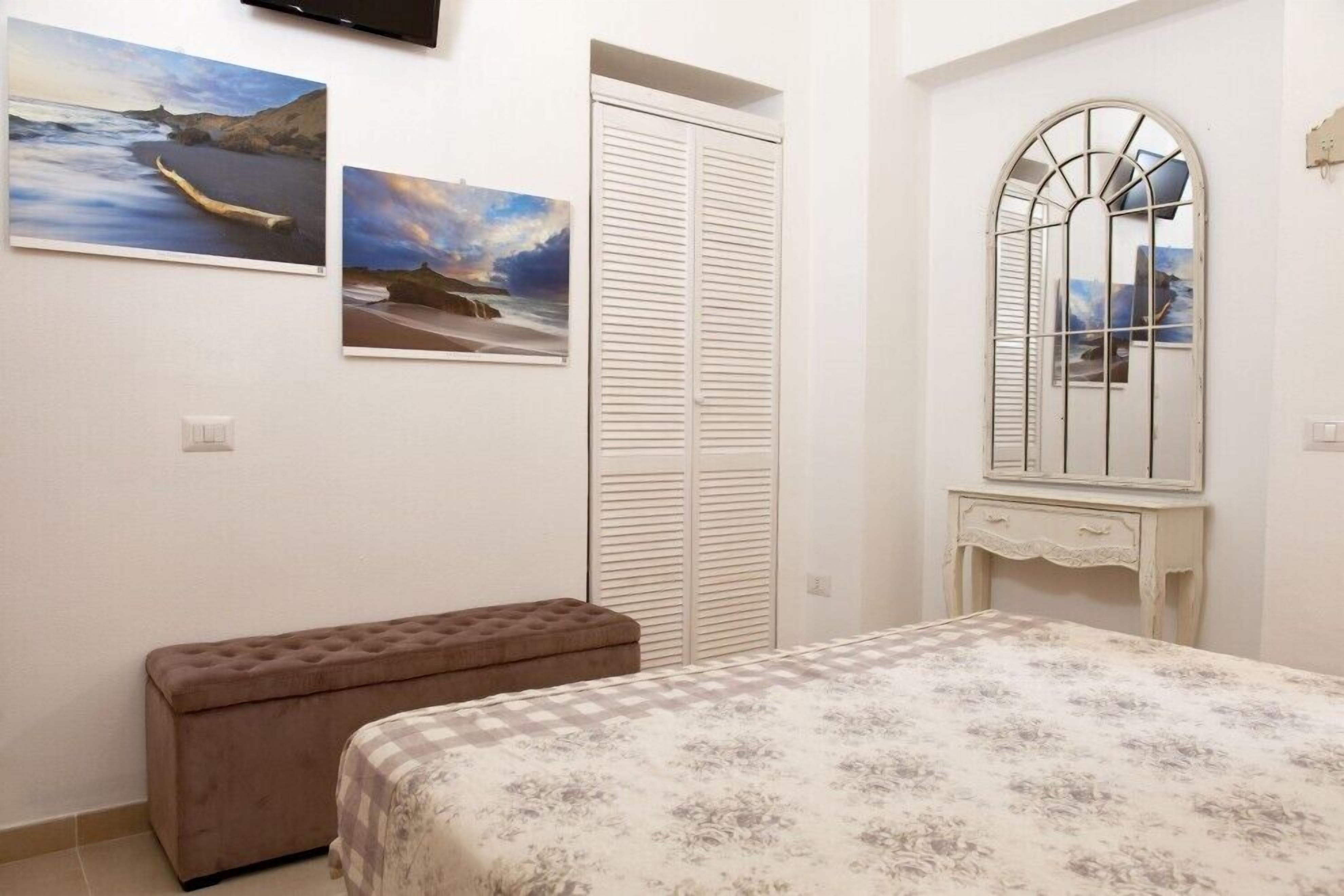 Un dormitorio con cama, un banco, un armario y dos cuadros en la pared.