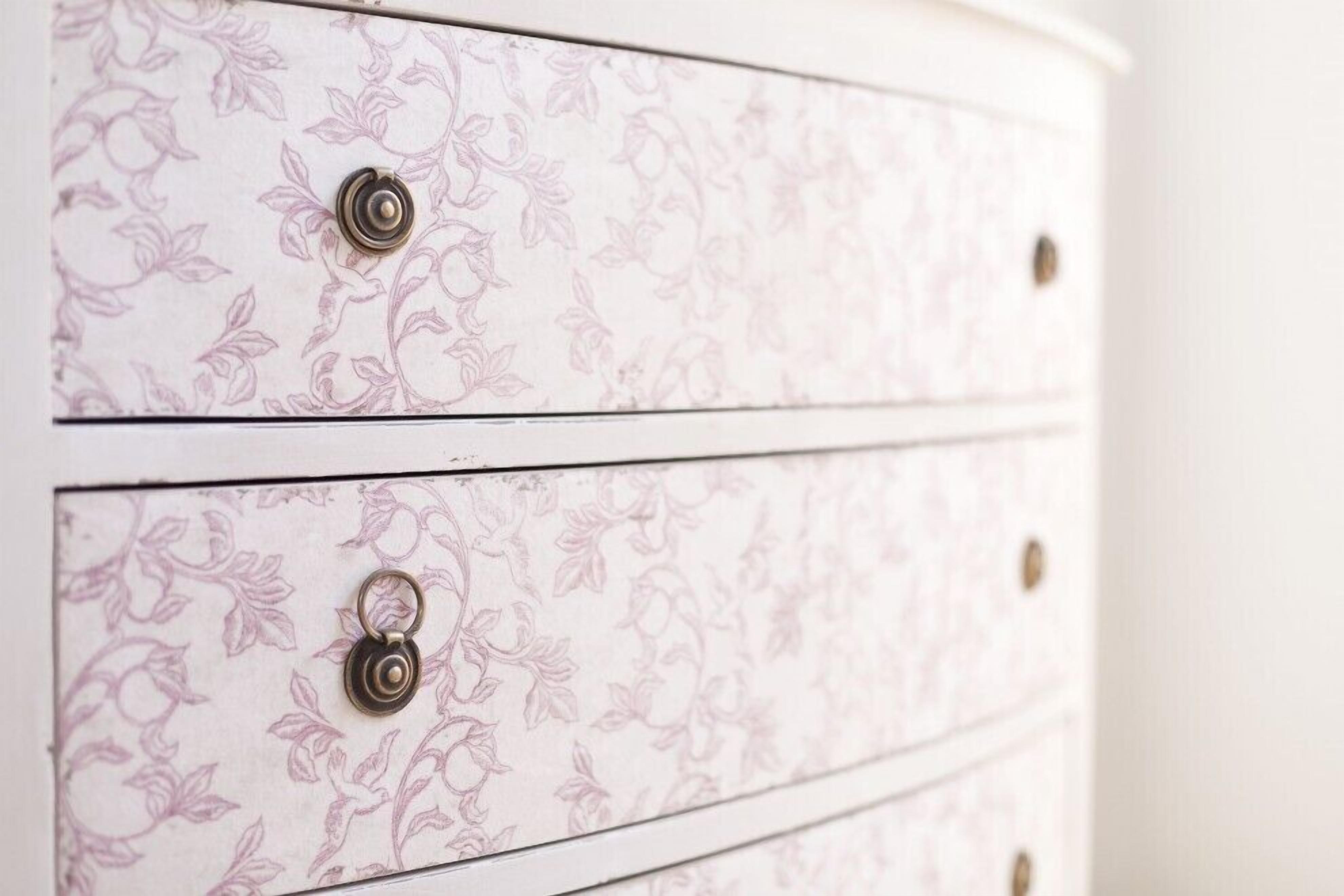 Une commode blanche ornée de motifs floraux et dotée de boutons métalliques.