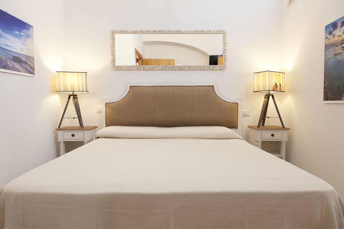 Quarto de hotel bem arrumado, com uma cama grande, duas mesas de cabeceira e duas luminárias.
