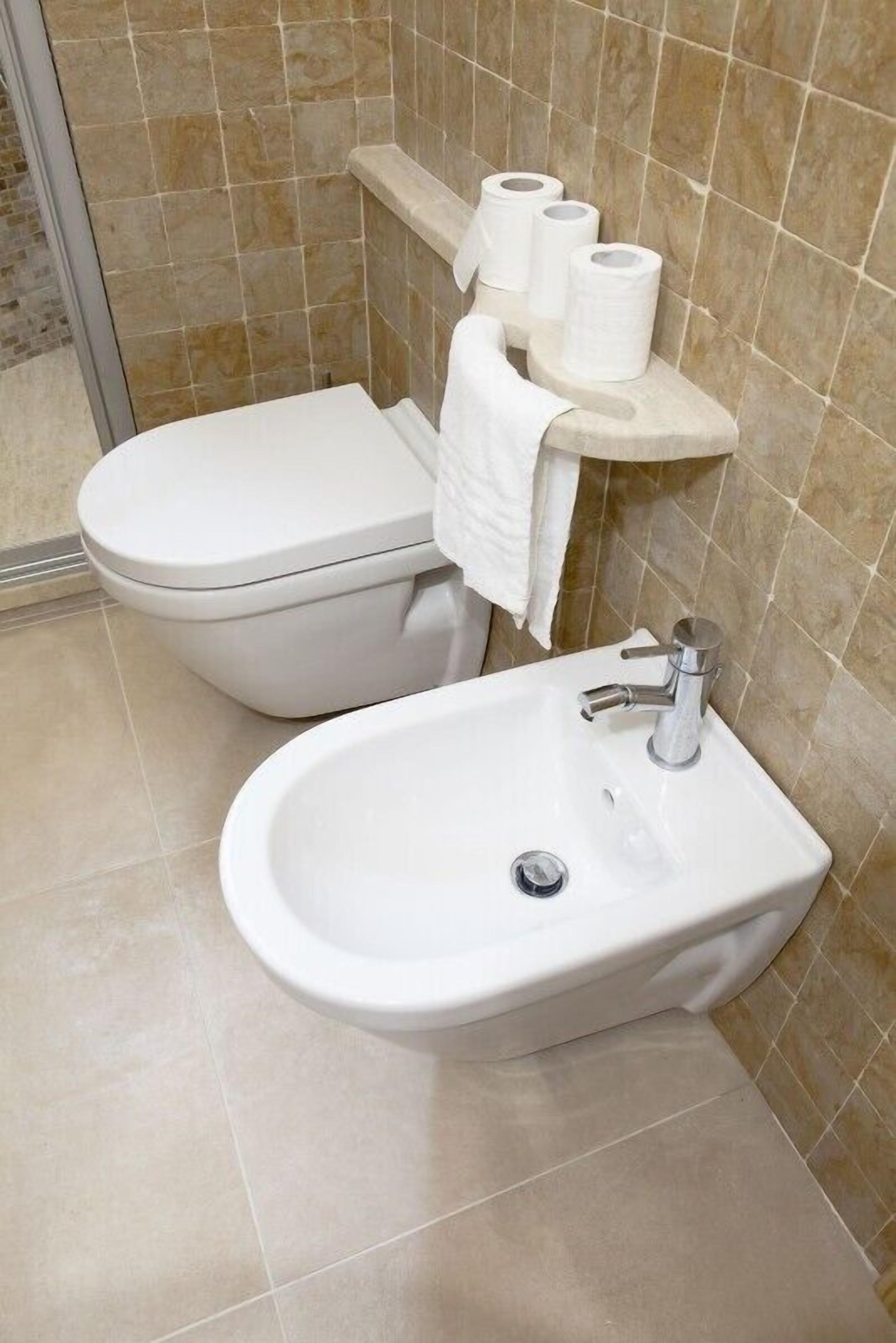Un baño con inodoro, lavamanos y repisa con papel higiénico y toalla.