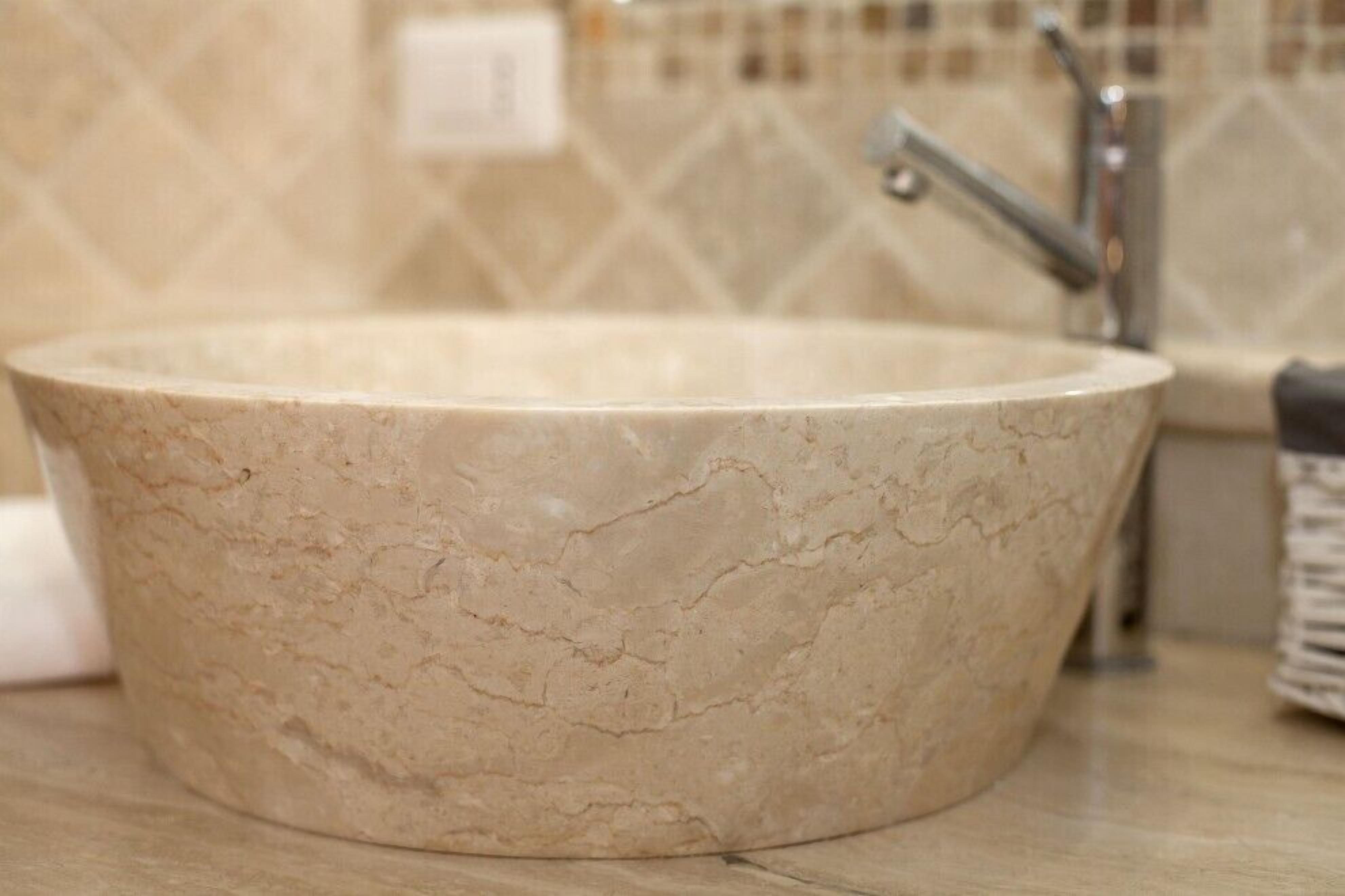 A round, beige marble sink with a faucet in a bathroom.