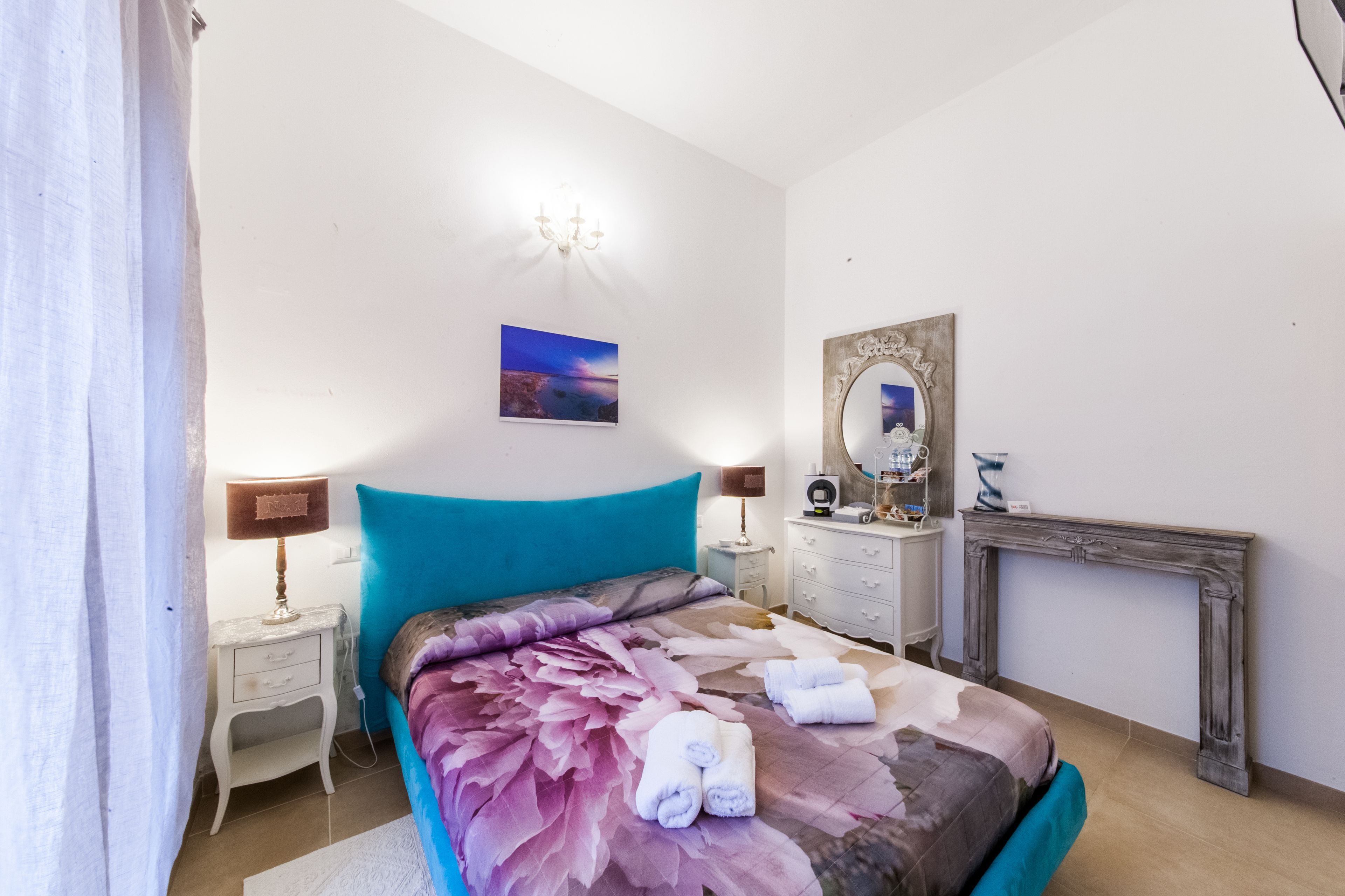 Un dormitorio con cama, mesitas de noche, cómoda, espejo y chimenea.
