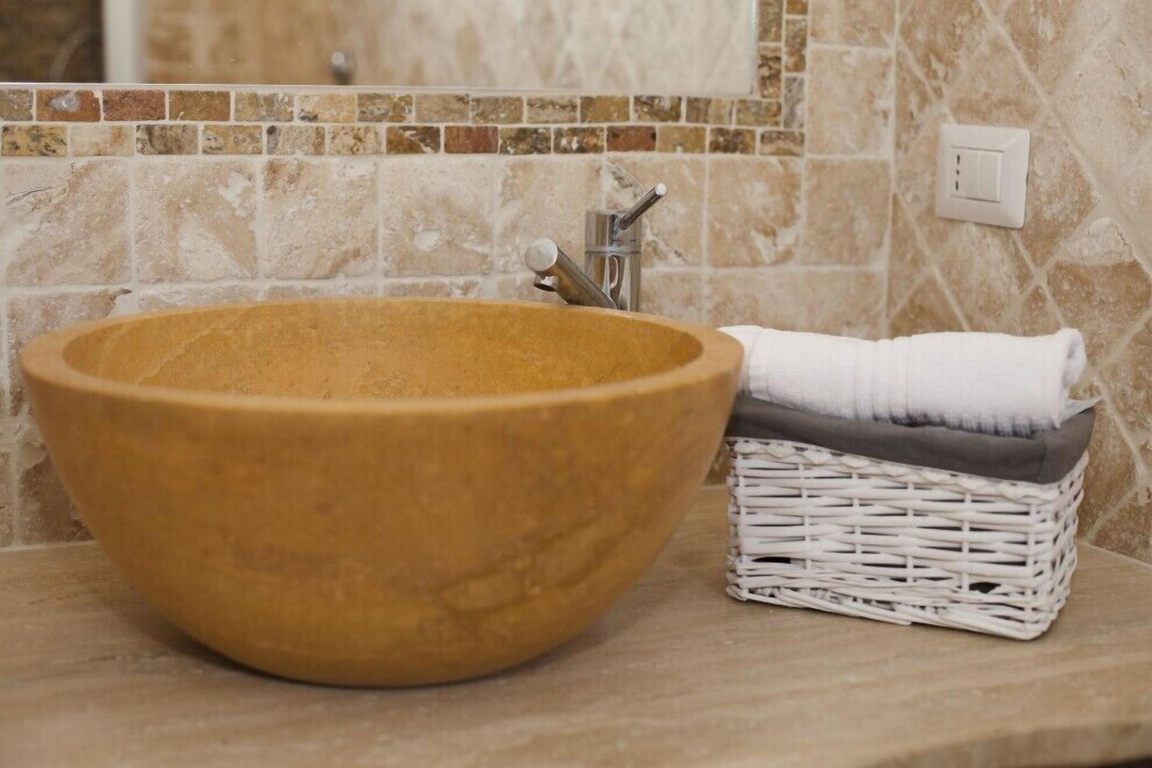 A bathroom with a large wooden bowl sink, a white wicker basket, and a towel.