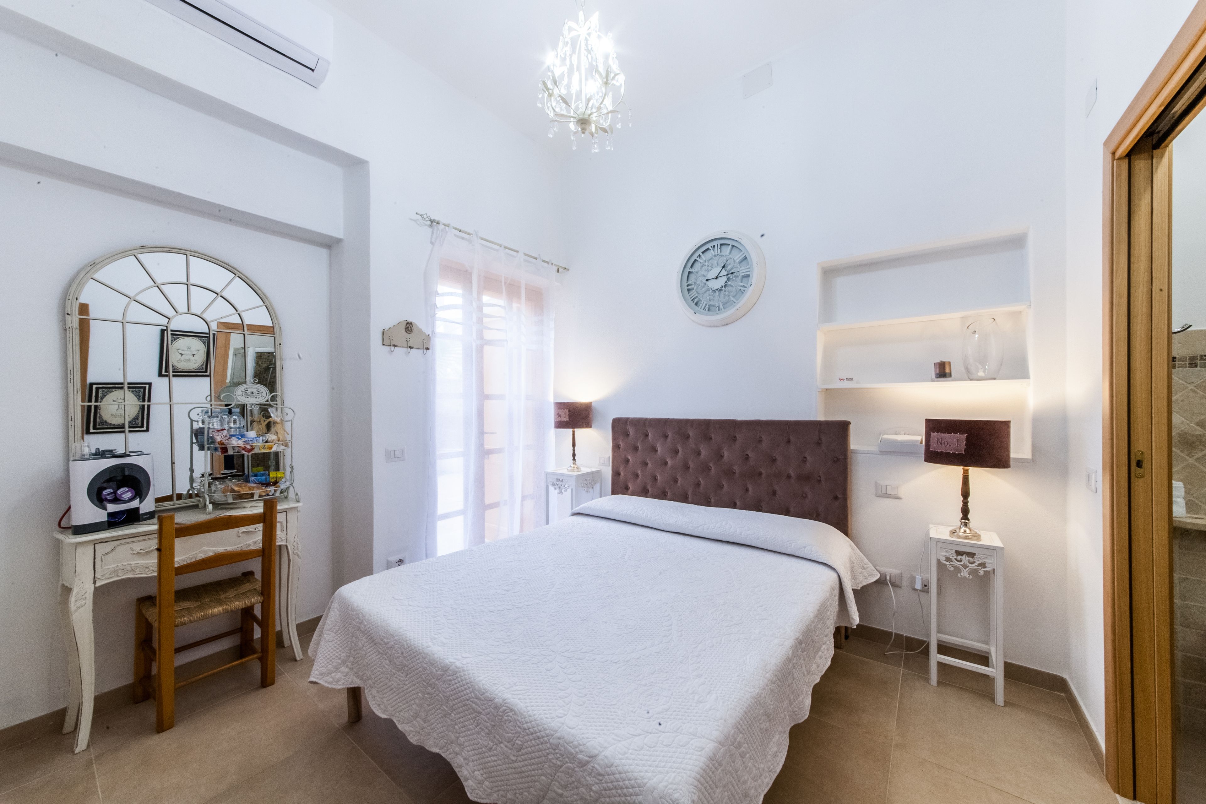 Une chambre à coucher comprenant un lit, une commode, un miroir, une horloge et un lustre.