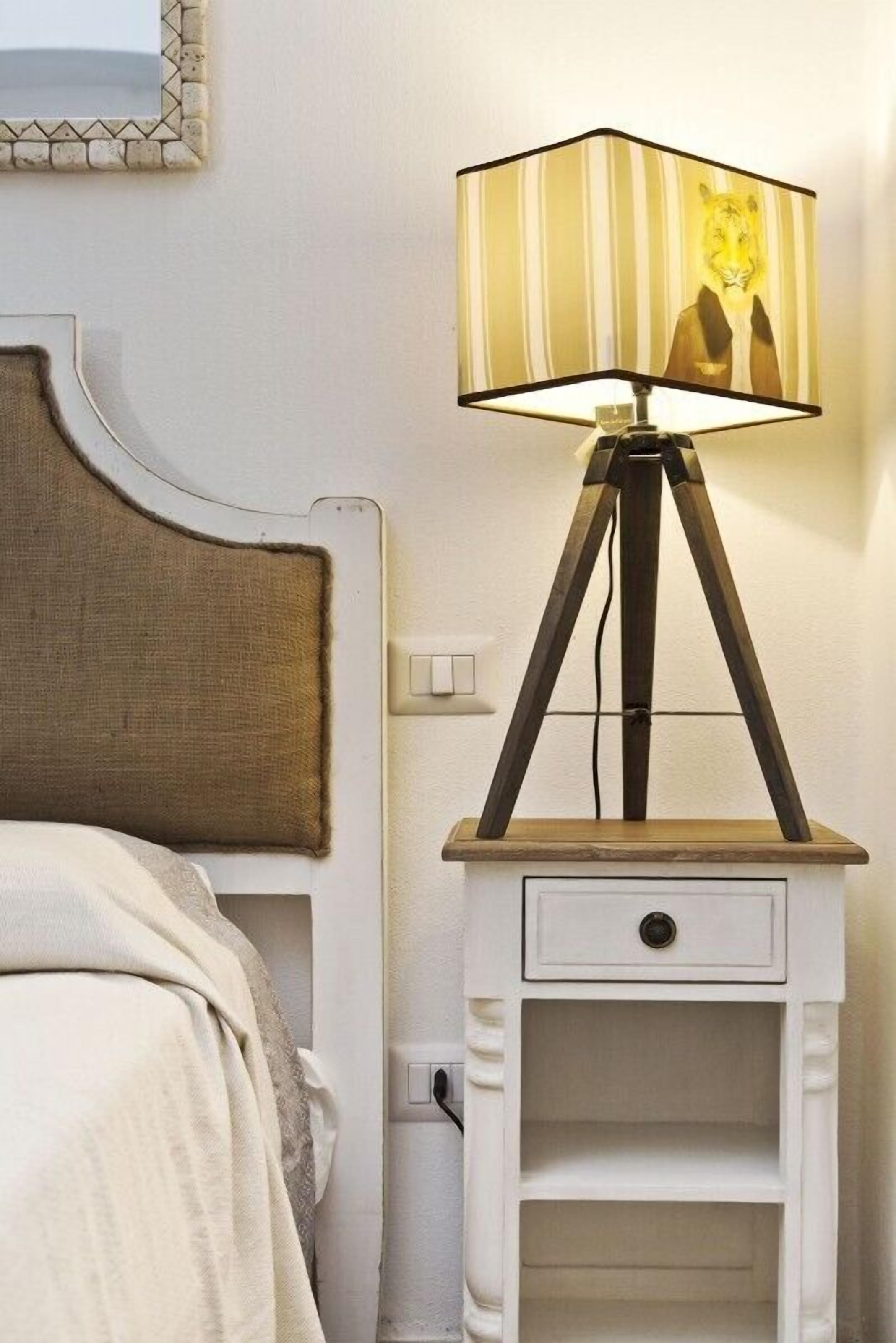 Ein Bett mit Kopfteil, ein Nachttisch mit Lampe und einem gestreiften Lampenschirm sowie eine kleine Schublade.