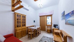 A compact living space with a red sofa, wooden cabinets, a dining table, and a TV. - Acuario Guest House (Oristano)