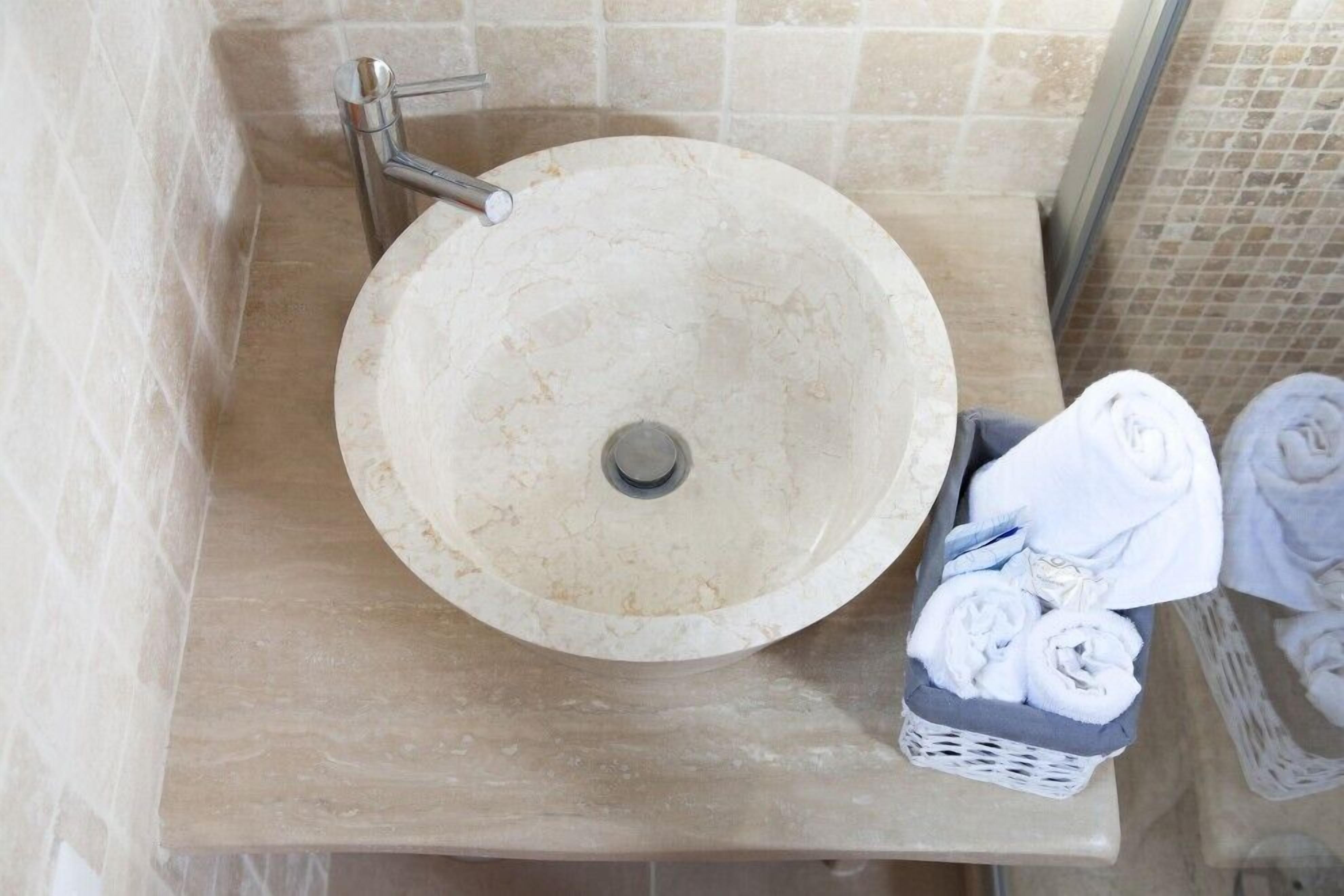 Un baño con un lavabo redondo, un perchero y una cesta de toallas.