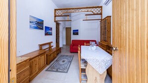 A room with a wooden dining table, a red sofa, and wooden cabinets. There are two paintings on the wall and a chandelier on the ceiling. - Acuario Guest House (Oristano)