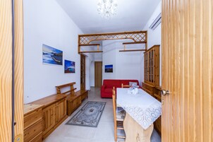Una habitación con una mesa de comedor de madera, un sofá rojo y armarios de madera. Hay dos cuadros en la pared y una lámpara de araña en el techo.