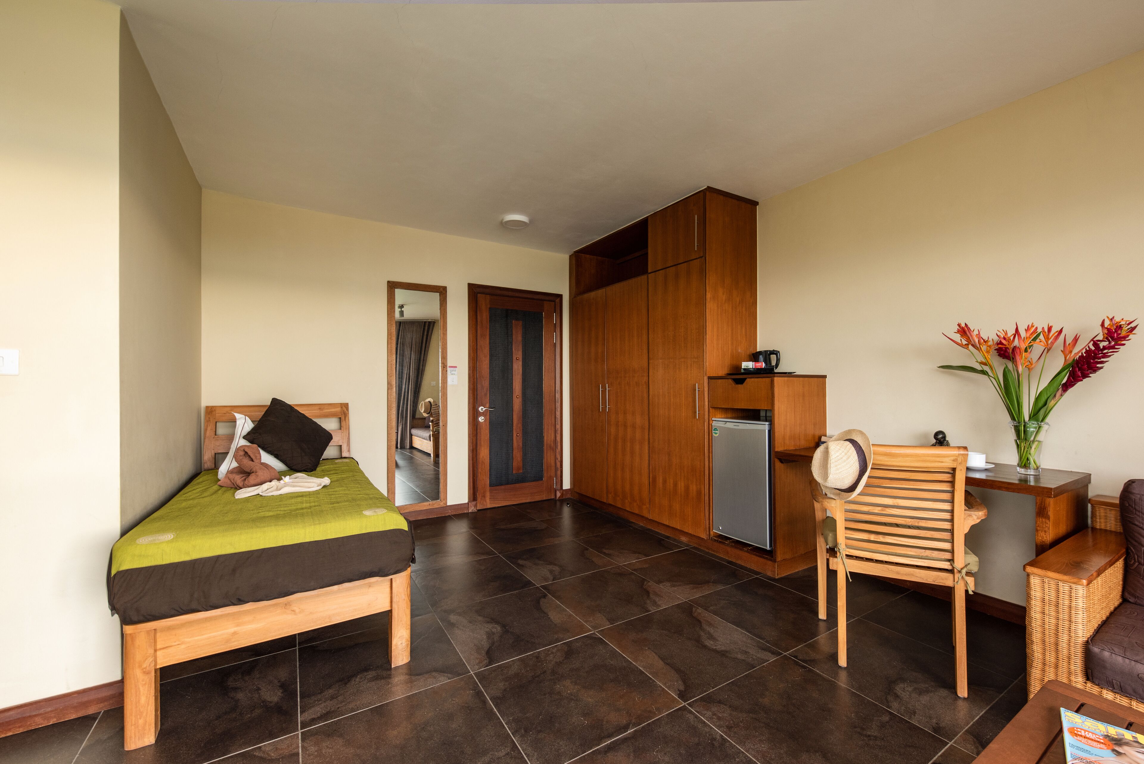 A room with a bed, a wooden wardrobe, a small kitchenette, a chair, and a table.
