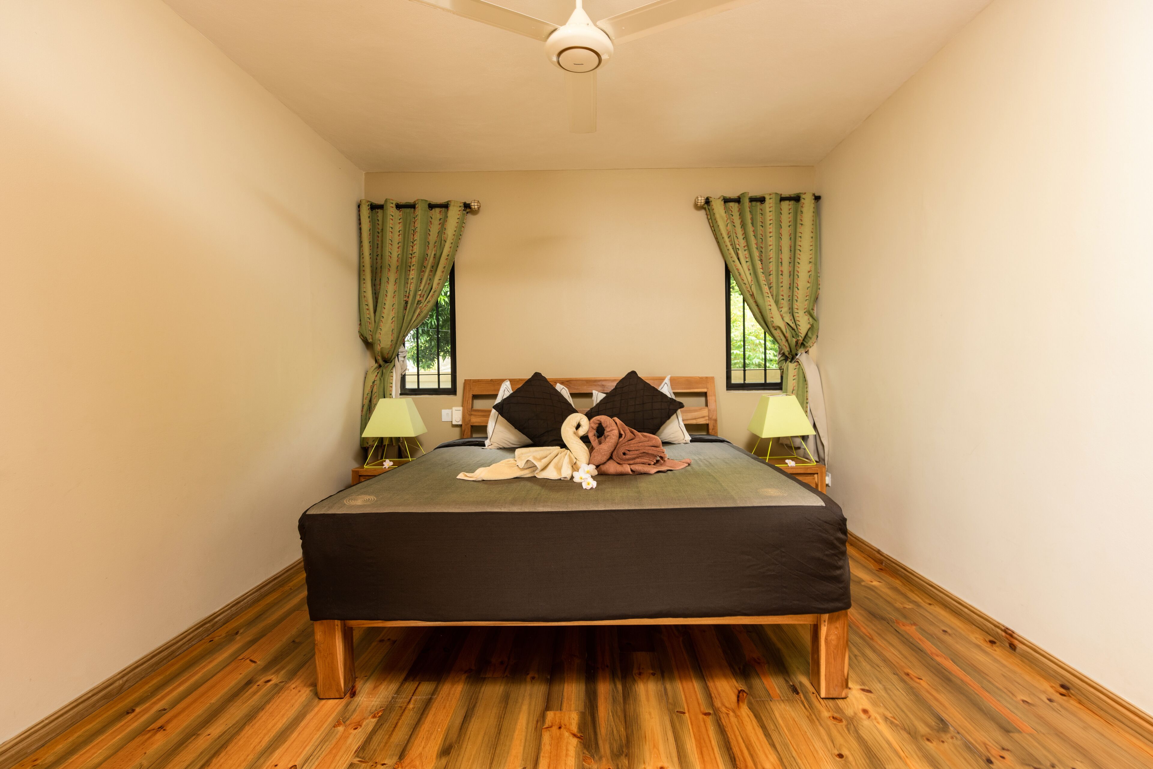 A bedroom with a wooden floor, a bed with a black bedspread, two pillows, a swan decoration, and curtains.