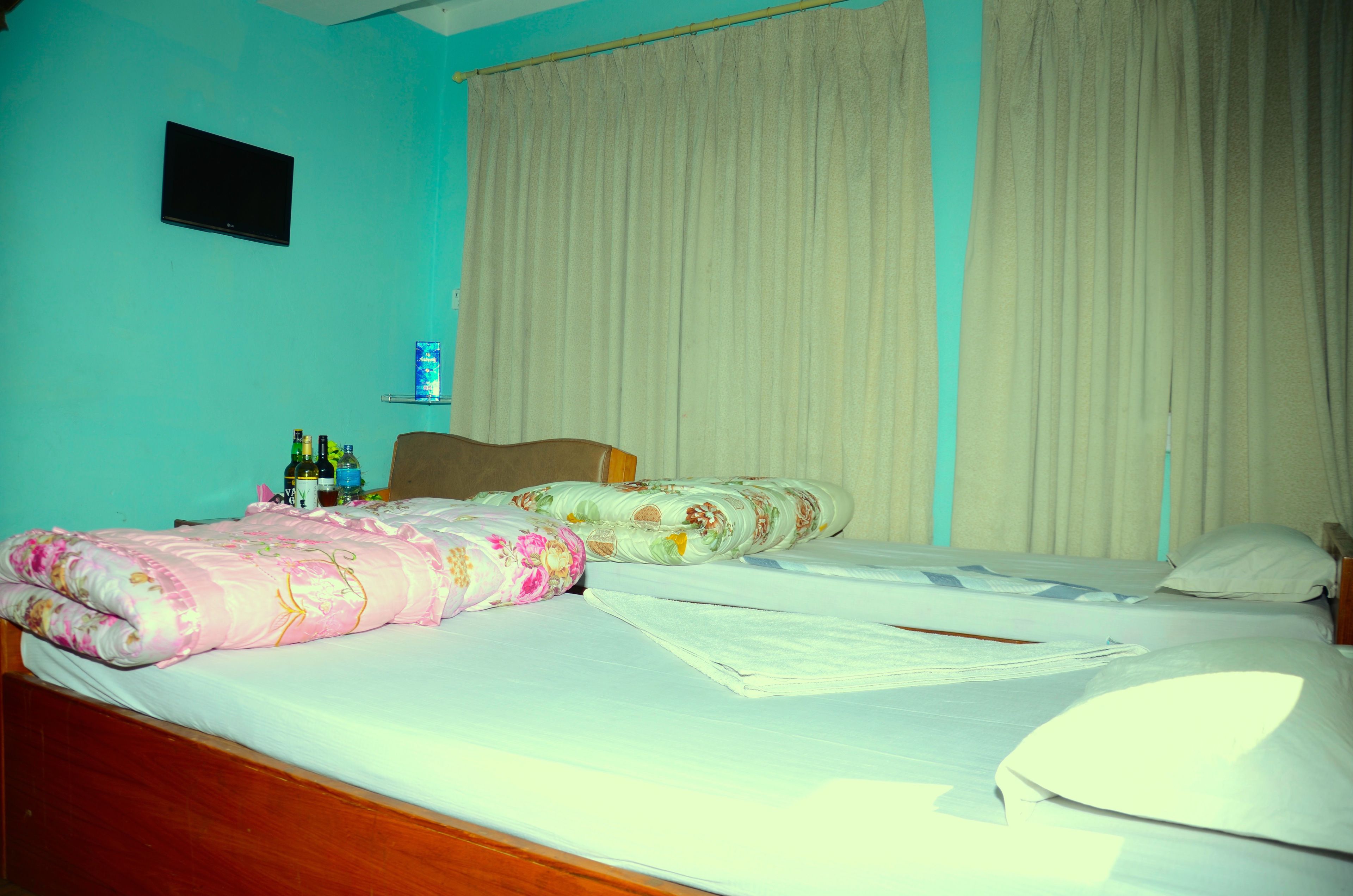 A hotel room with two beds, a TV on the wall, and a shelf with toiletries.