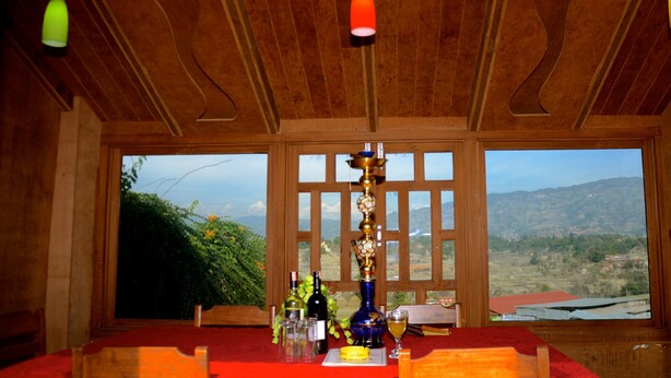 Un comedor con una mesa dispuesta para dos personas, vistas a las montañas a través de grandes ventanales y un techo de madera con un diseño único.