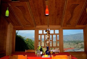 Un comedor con una mesa dispuesta para dos personas, vistas a las montañas a través de grandes ventanales y un techo de madera con un diseño único.