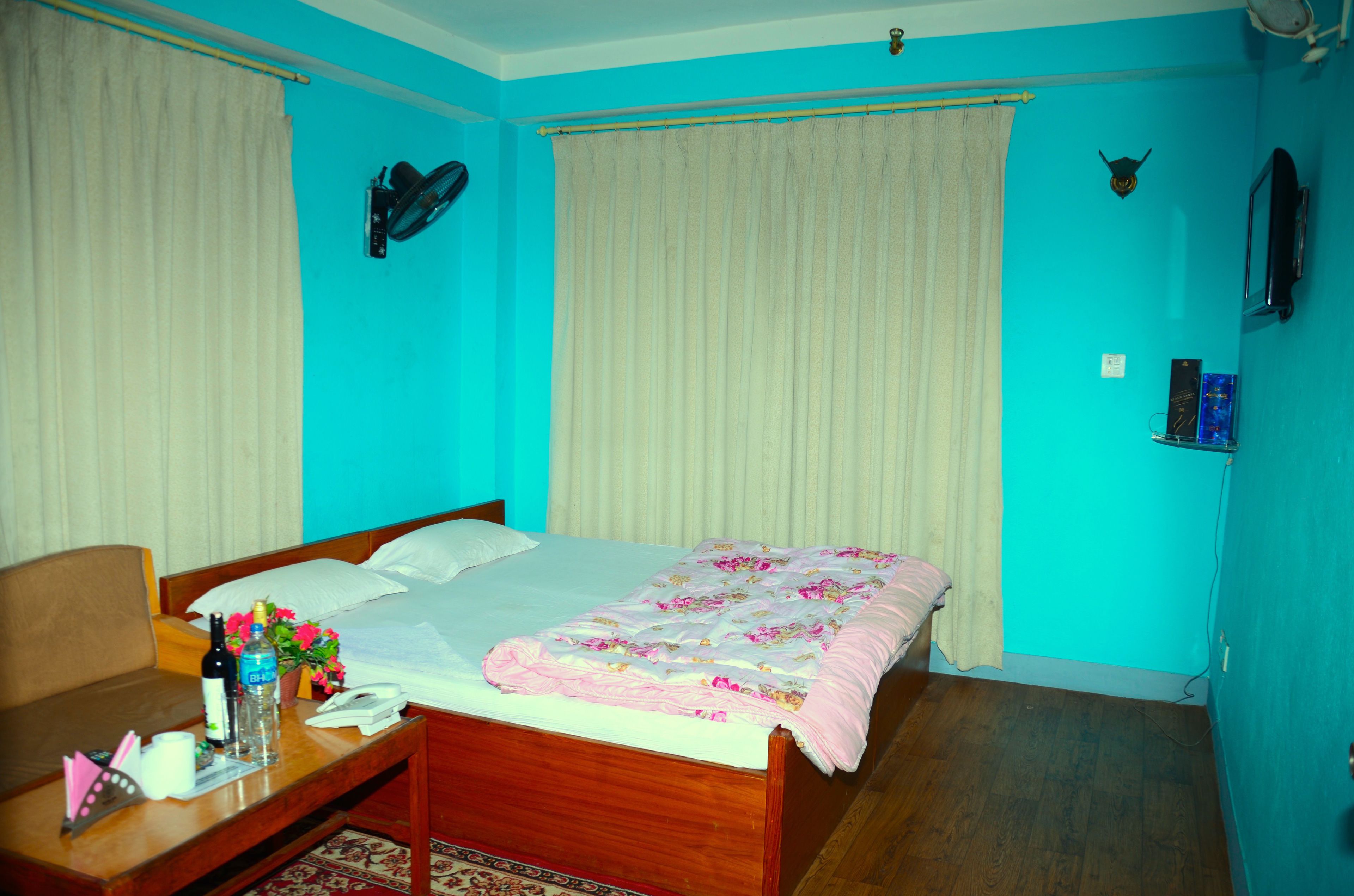 Un dormitorio con una cama de madera, una mesita de noche con una botella, un teléfono y un jarrón con flores.