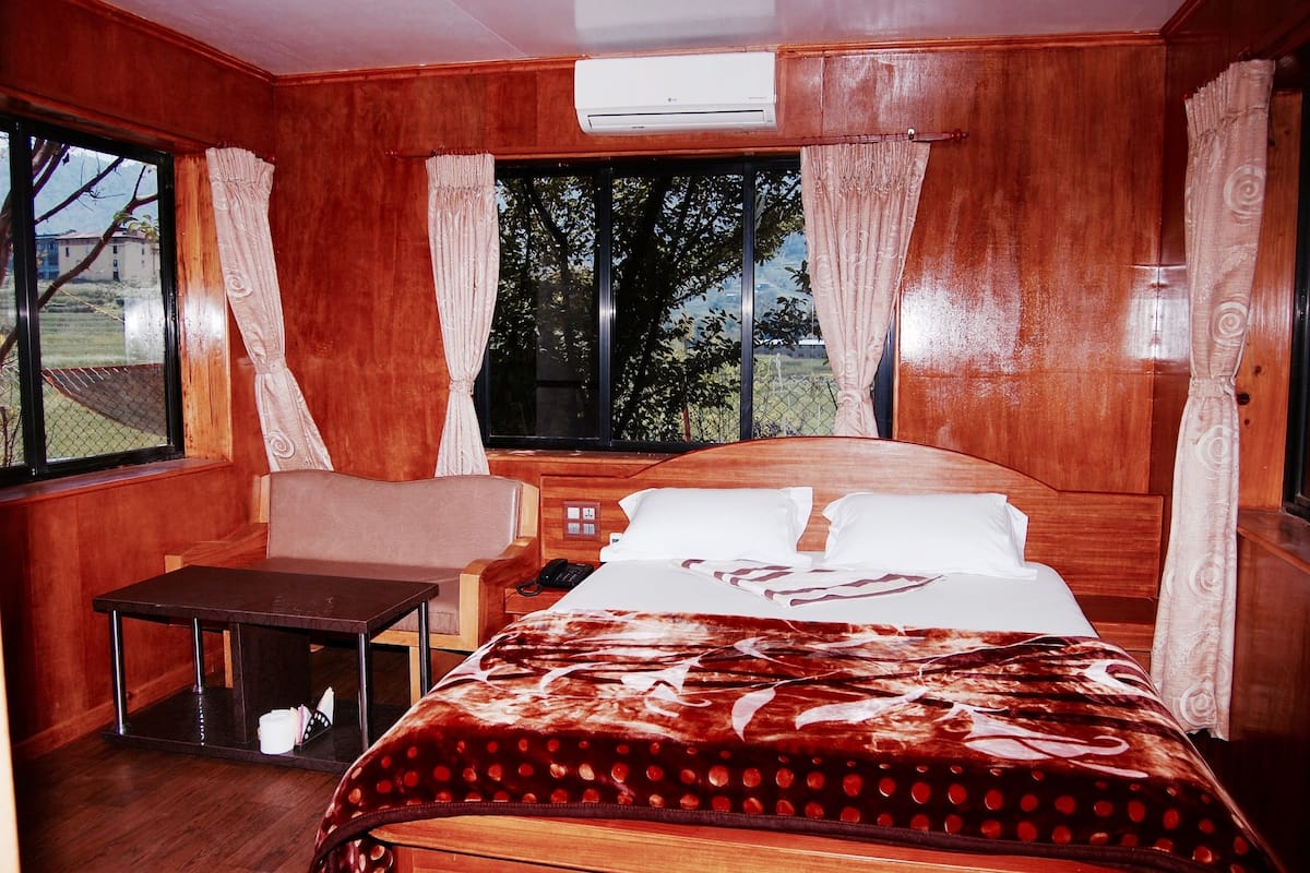 A wooden room with a bed, a small table, and a window with curtains.