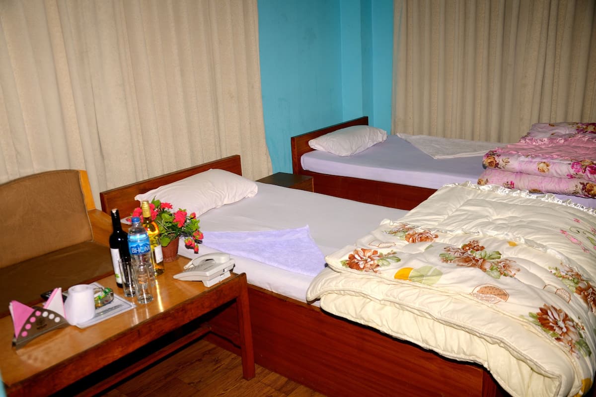 A hotel room with two beds, a wooden desk, a telephone, and a small table with a bottle, glasses, and a flower vase.