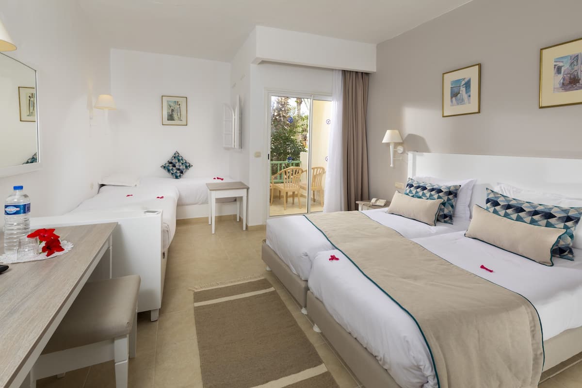 A hotel room with a bed, a desk, a chair, a small table, and a balcony.