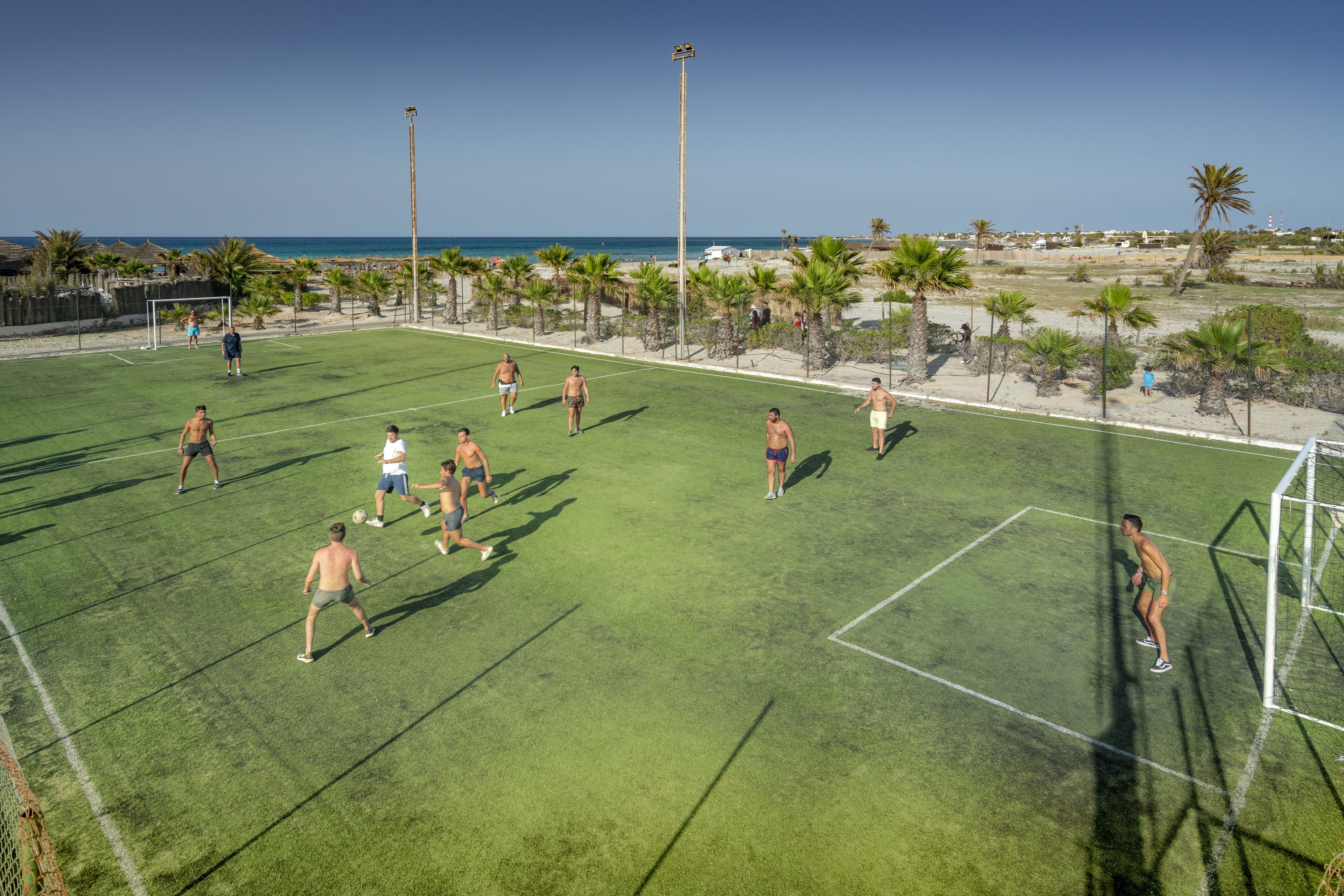 Ein Sportplatz im Freien mit einem Tor, umgeben von Palmen und wolkenlosem Himmel.