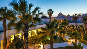 A hotel courtyard with palm trees, a well-lit building, and a dome structure in the background. - Yadis Djerba Thalasso & Golf (Djerba Midun)