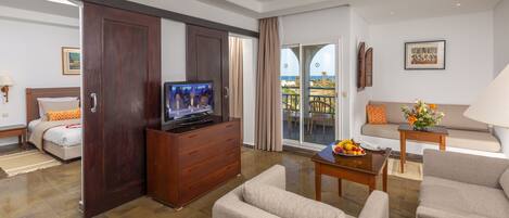 Habitación de hotel con balcón, televisión, sofá, mesa de comedor y cama.