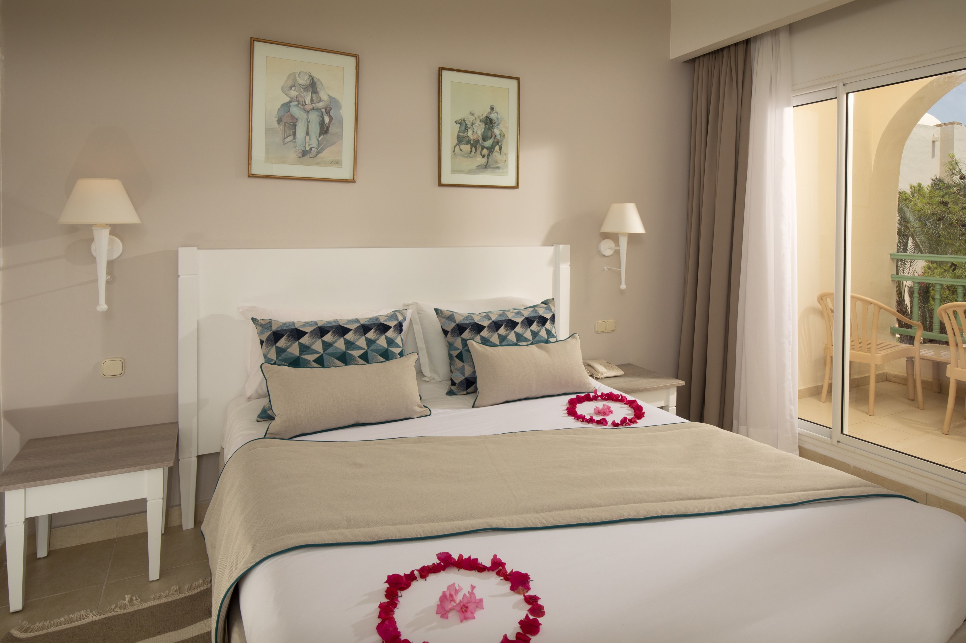 Une chambre d’hôtel avec un grand lit, deux tables de chevet, une petite table et une vue sur le balcon extérieur.