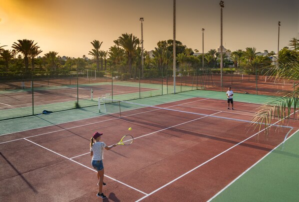 A tennis court with a net, two players, and palm trees in the background.