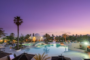 A resort pool area with palm trees, lounge chairs, umbrellas, and a dome-shaped building in the background.
