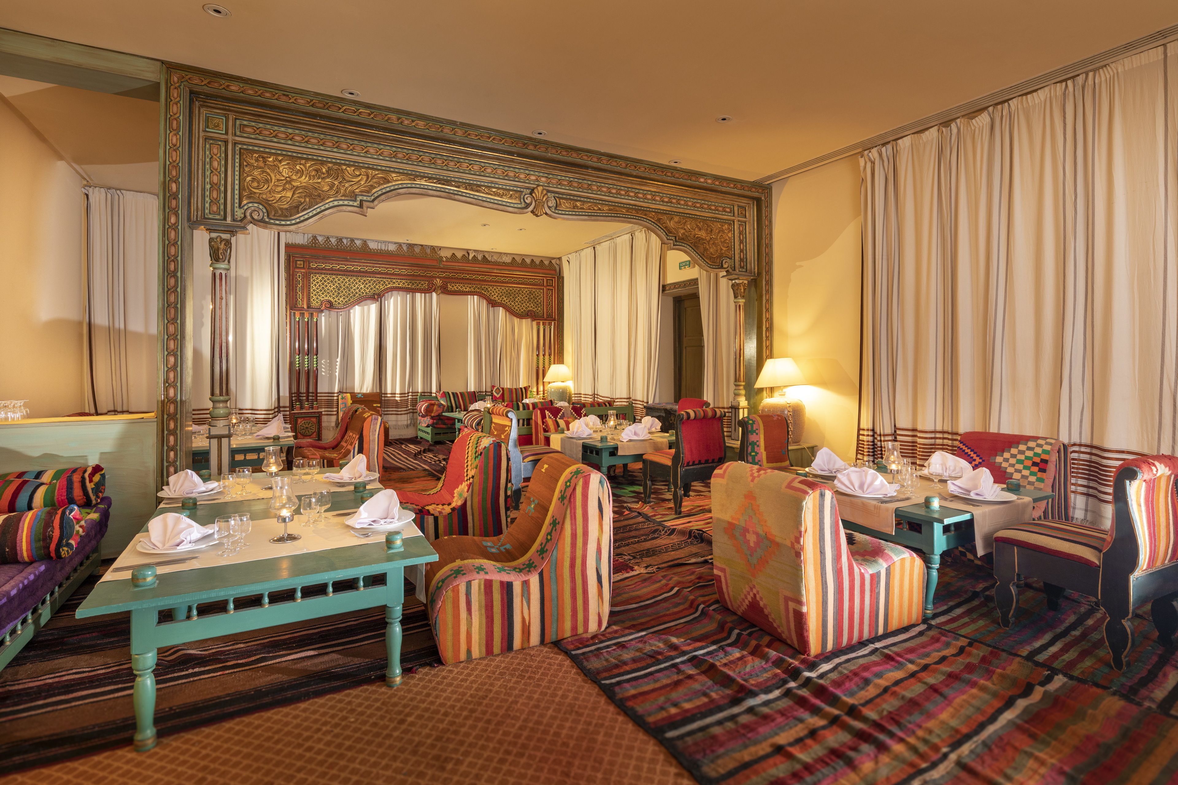 A hotel room with a large mirror, striped upholstered chairs, a teal coffee table, and a patterned carpet.