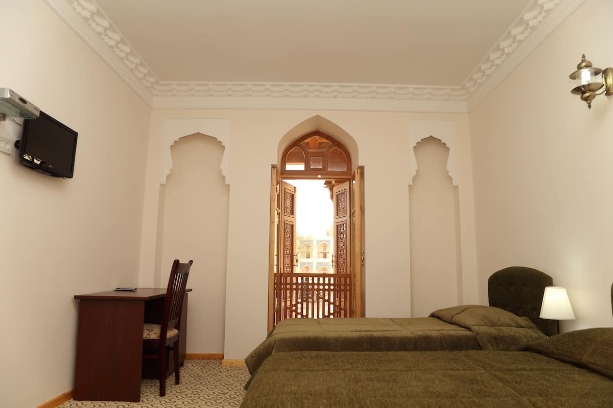 A bedroom with a bed, a desk, and a chair. There is a TV mounted on the wall and a lamp on the side table.