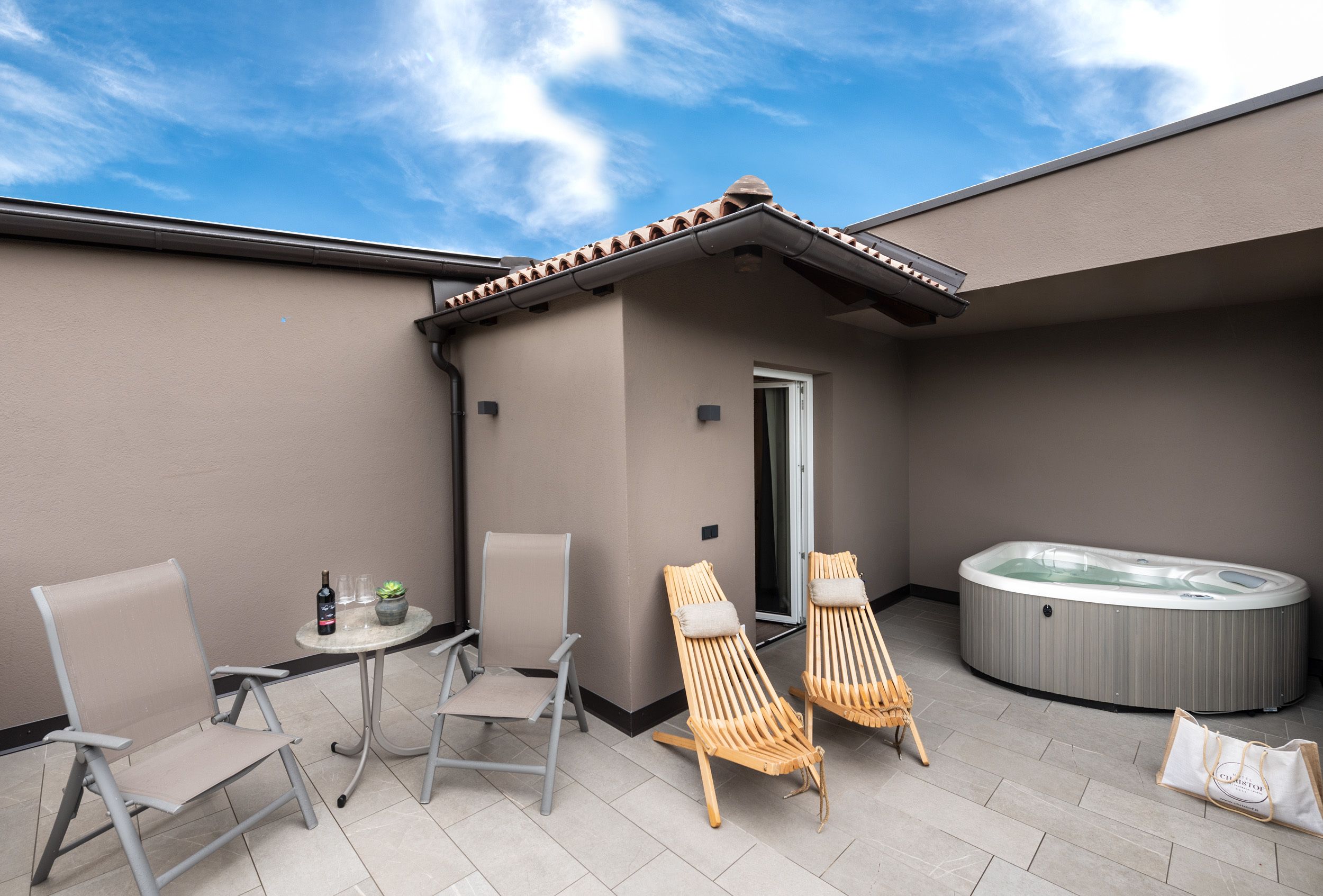 Un espace patio comprenant deux chaises longues, un jacuzzi et une petite table avec une bouteille et des verres.
