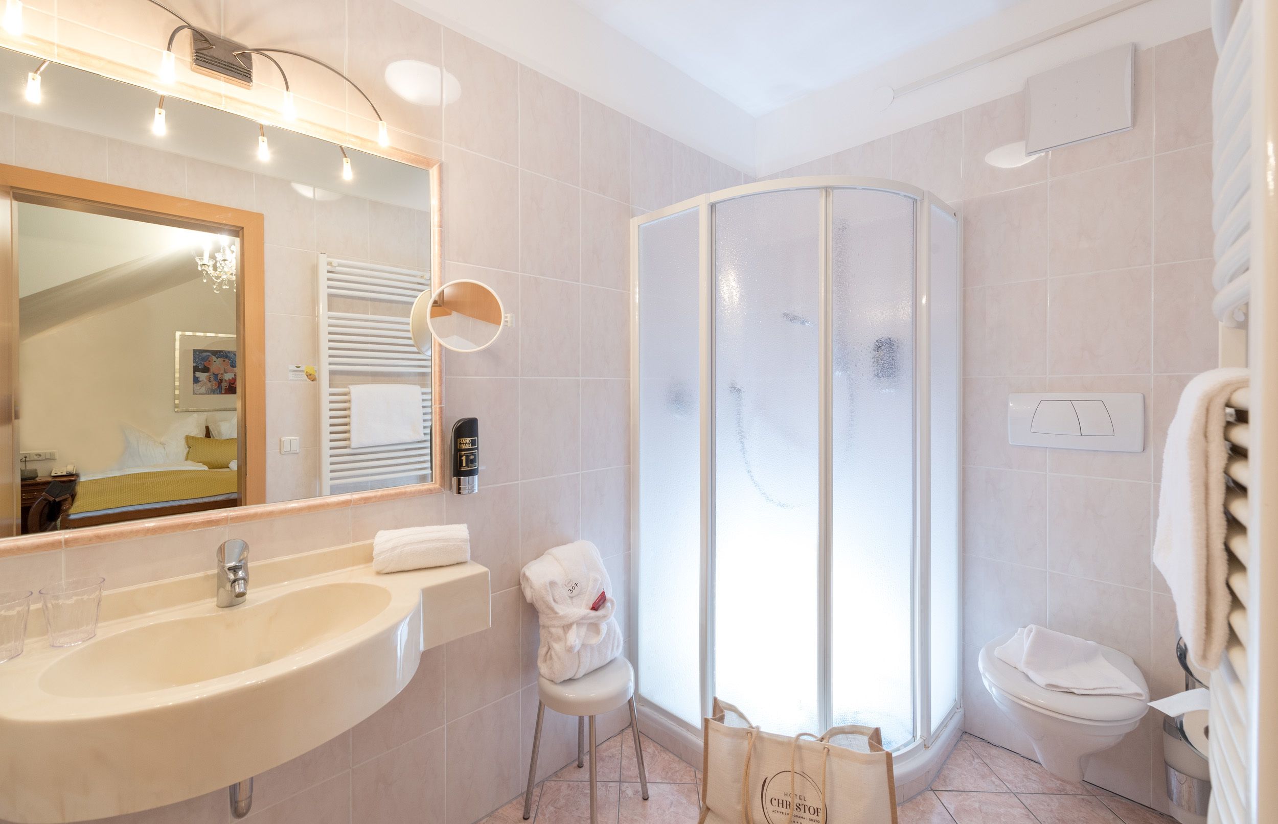 A bathroom with a sink, mirror, towel rack, shower enclosure, toilet, and a bag on the floor.