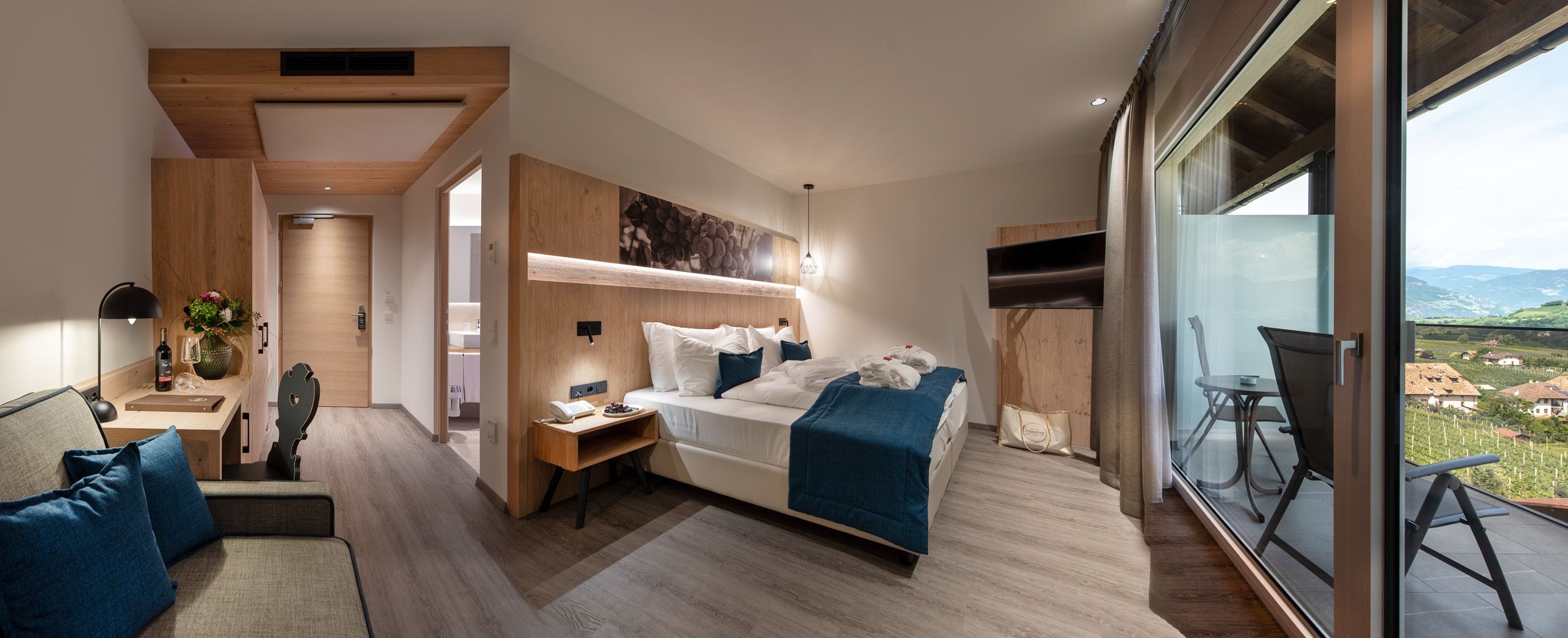 Ein modernes Hotelzimmer mit Bett, Schreibtisch, Sofa und einem Balkon mit Blick.