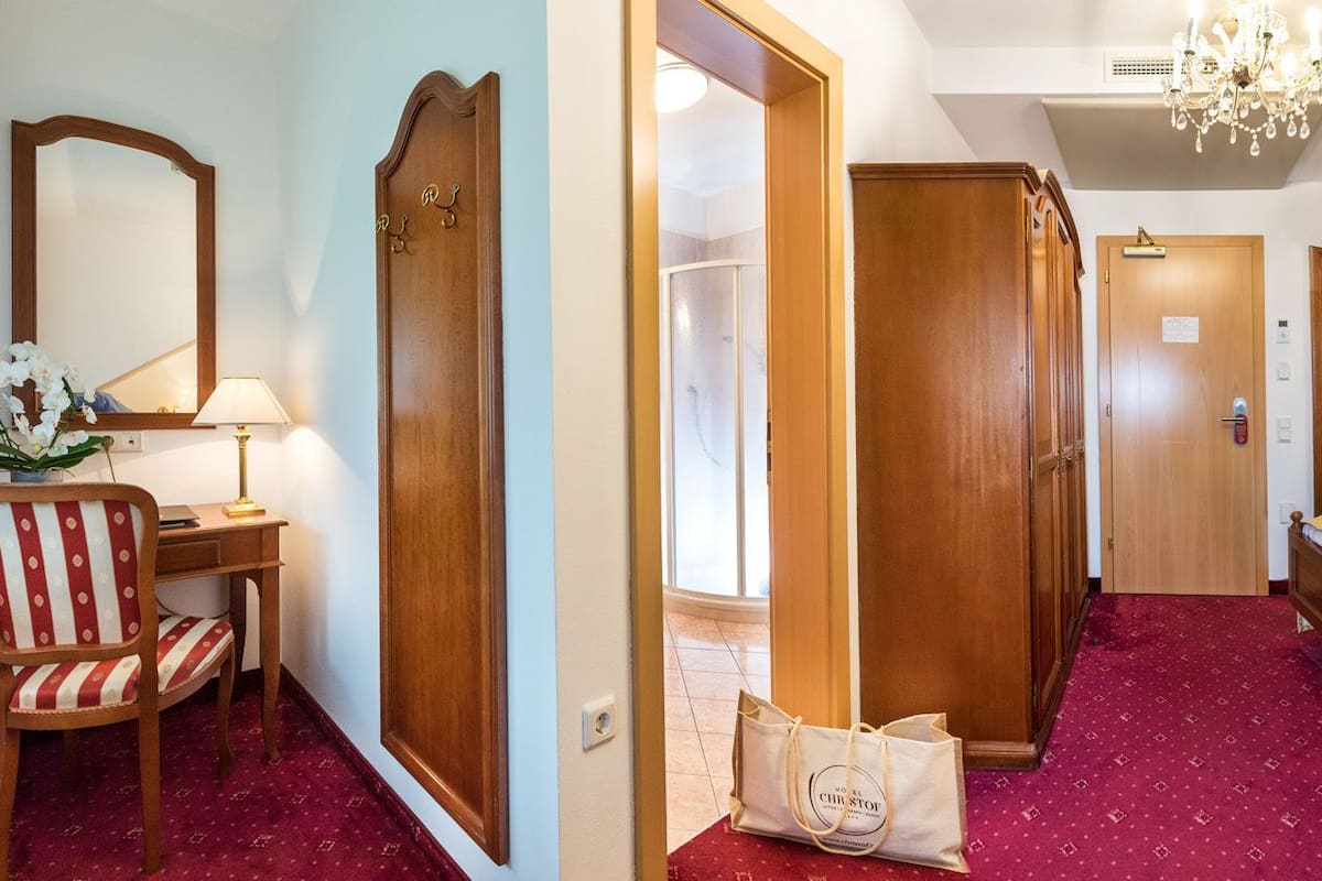 Une chambre d’hôtel avec un grand lit, un bureau avec une chaise, un miroir et un lustre.