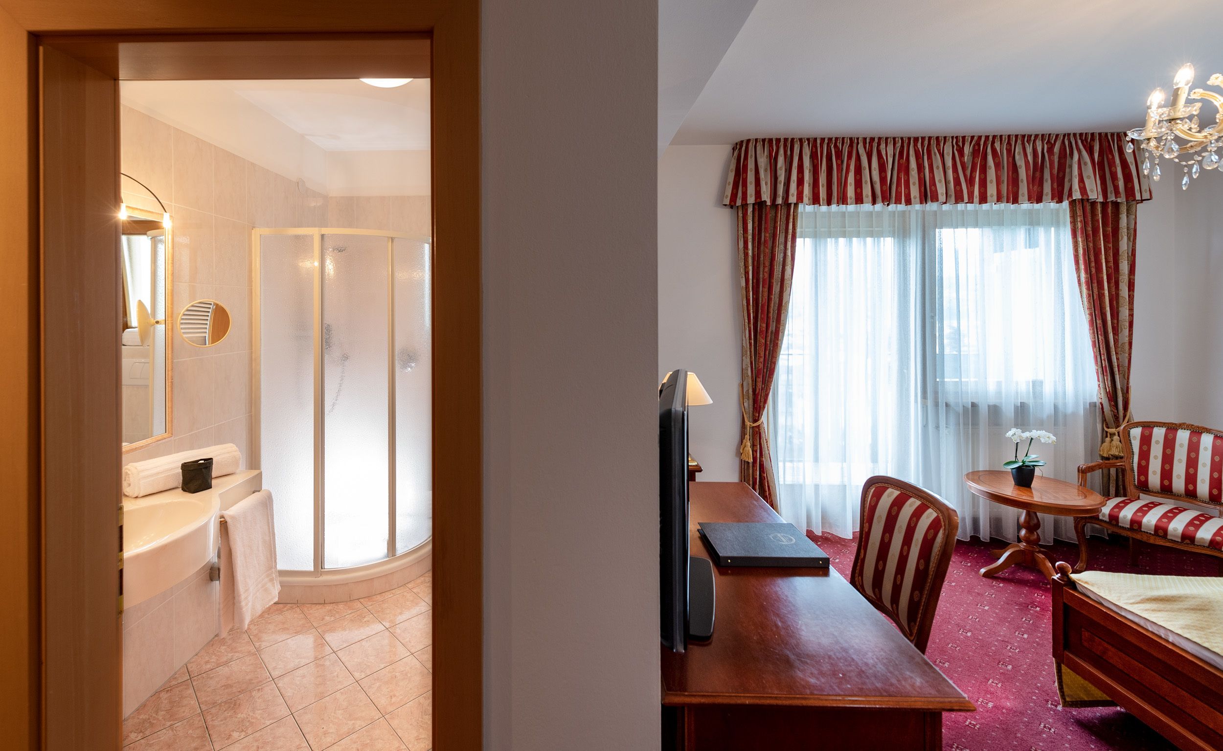 A hotel room with a bathroom, a sitting area with a table and chairs, and a bed.