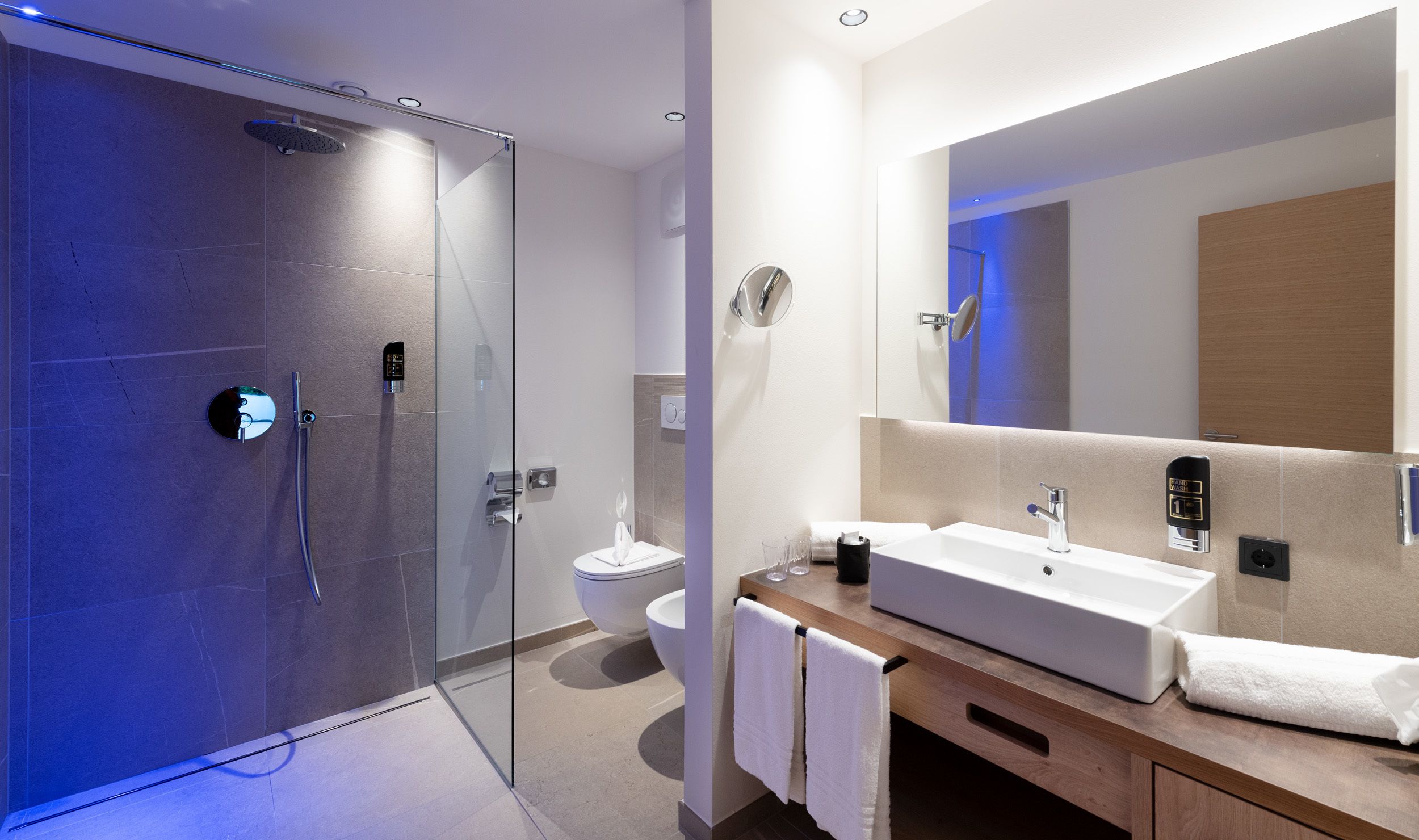 Un baño moderno con ducha de vidrio, lavamanos blanco y un espejo grande.